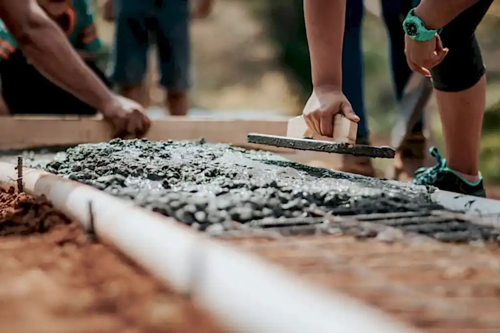 Construction workers leveling fresh cement on a sunny day at an outdoor site.